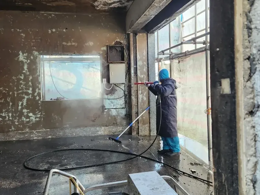유리창 샷시 화재청소 그을음 세척 작업 공정 사진, 넓은 실내에서 고압 세척기로 그을린 천장과 벽을 세척하는 작업자 — 유리창 샷시 화재청소 그을음 세척